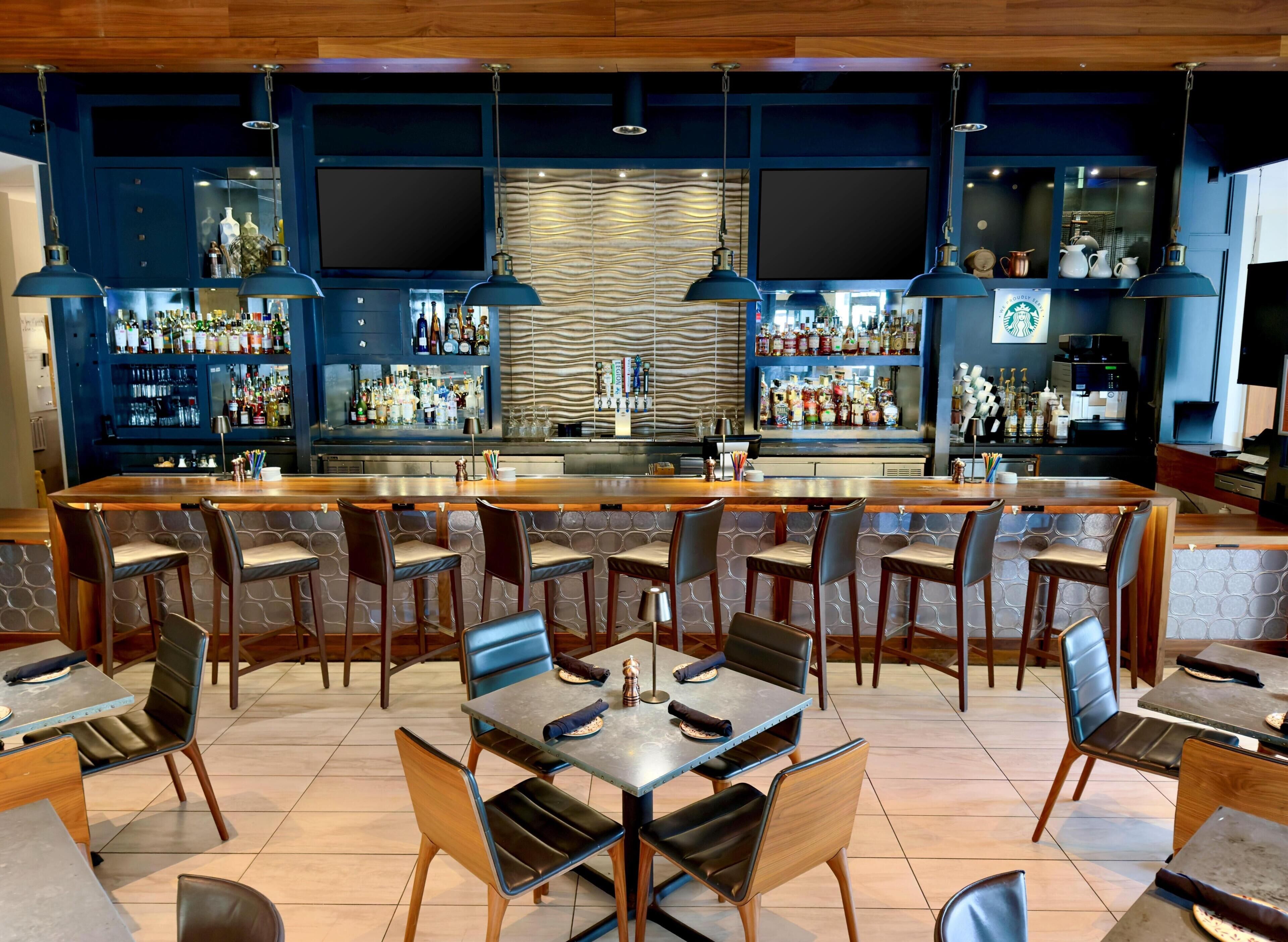 A bar area with multiple seating options, a bar counter, and shelves stocked with bottles.