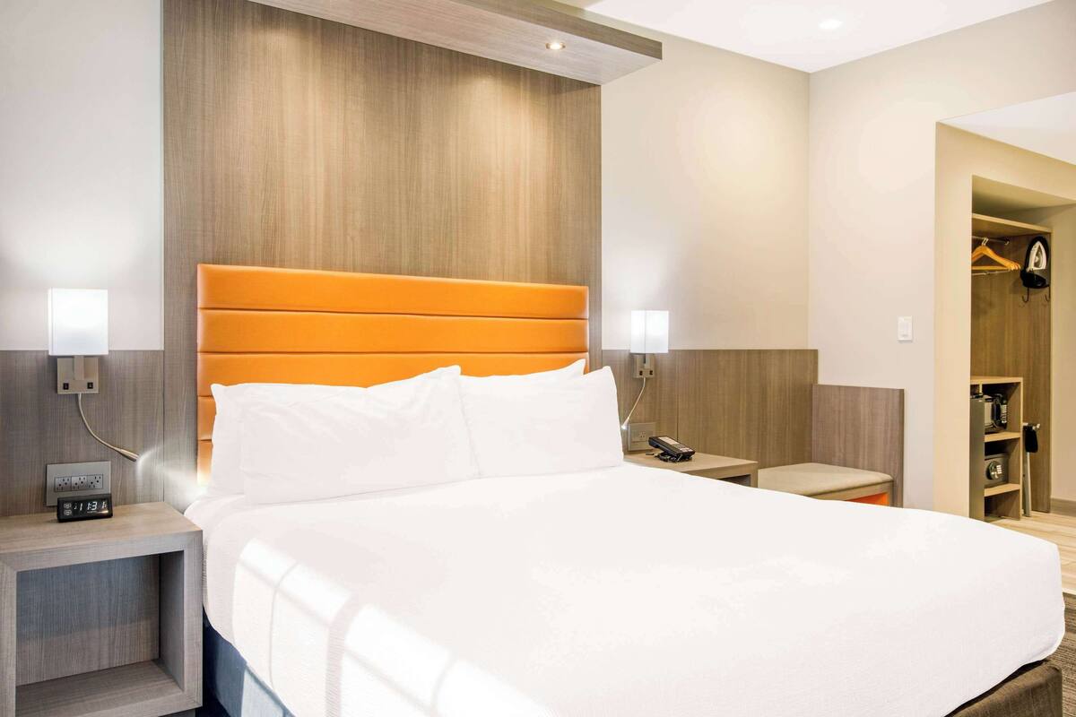 A hotel room with a large bed, wooden headboard, bedside tables with lamps, and a wardrobe with hanging clothes.