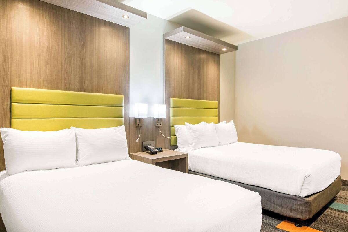 A hotel room with two beds, wooden headboards, a nightstand with a phone, and a mirror.