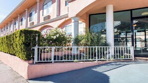 A pink building with large windows, a white fence, and greenery. - Rodeway Inn near Melrose Ave (Los Angeles)