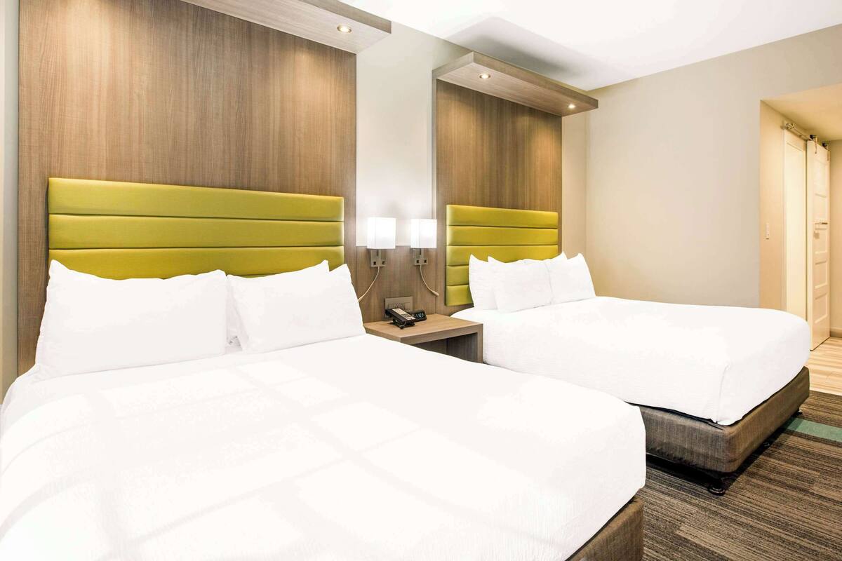 A hotel room with two beds, wooden headboards, a nightstand with a lamp, and a mirror.