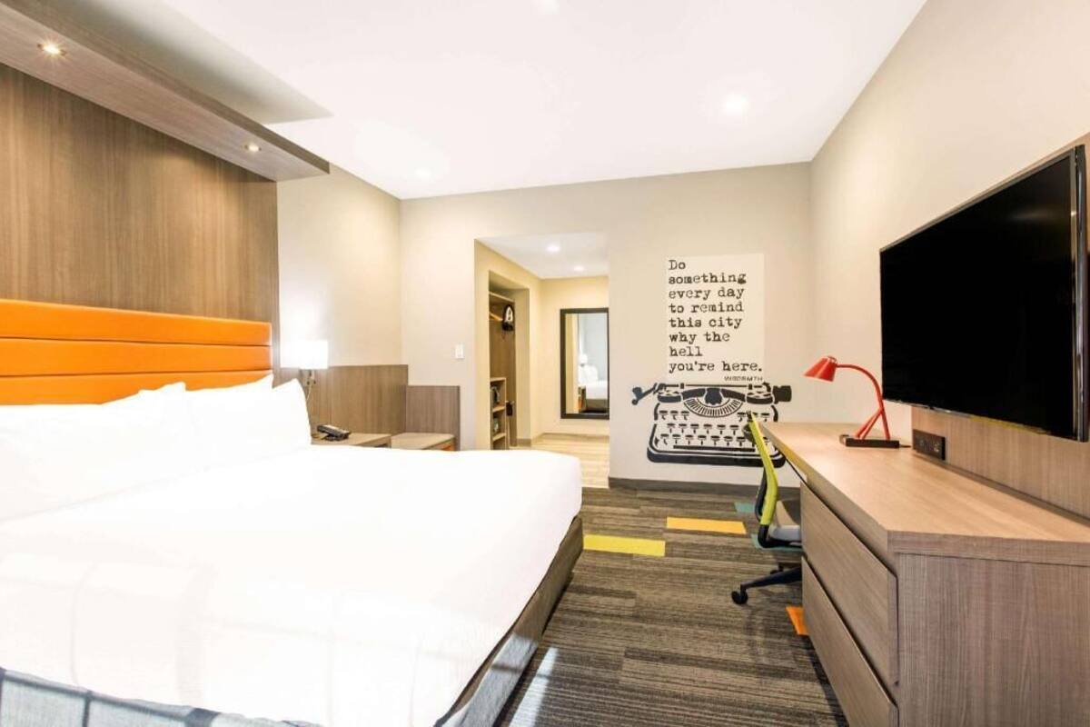 A hotel room with a bed, a desk, a TV, and a motivational poster on the wall.