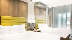 A hotel room with two beds, a wooden headboard, a nightstand with lamps, and a large window with curtains. - Rodeway Inn near Melrose Ave (Los Angeles)