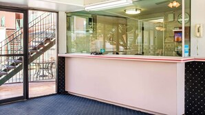 A reception area with a glass partition, a desk, a telephone, and a clock on the wall. - Rodeway Inn near Melrose Ave (Los Angeles)