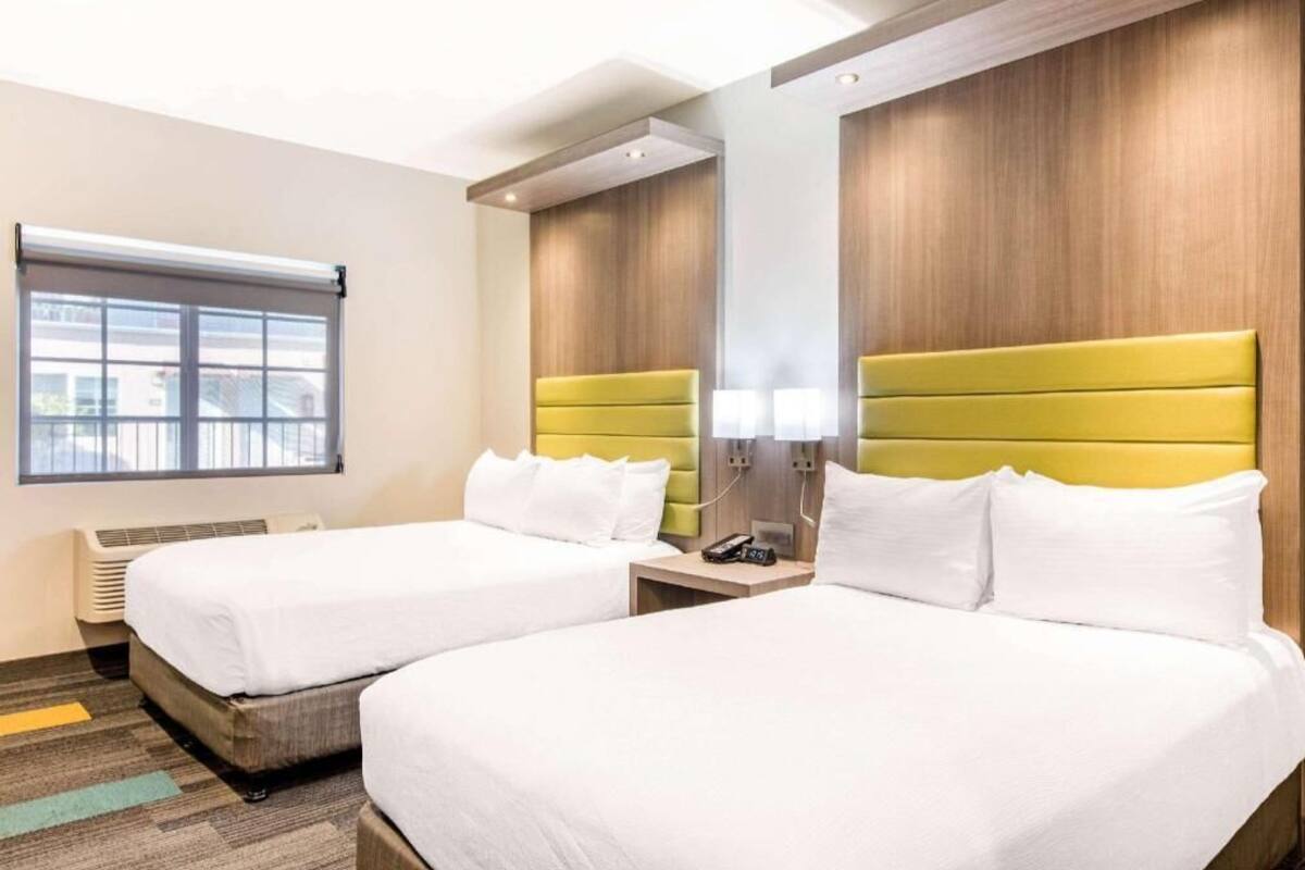 A hotel room with two beds, a window, a wall-mounted phone, and a bedside table.