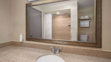Un baño con un espejo grande, un lavamanos y una zona de ducha.