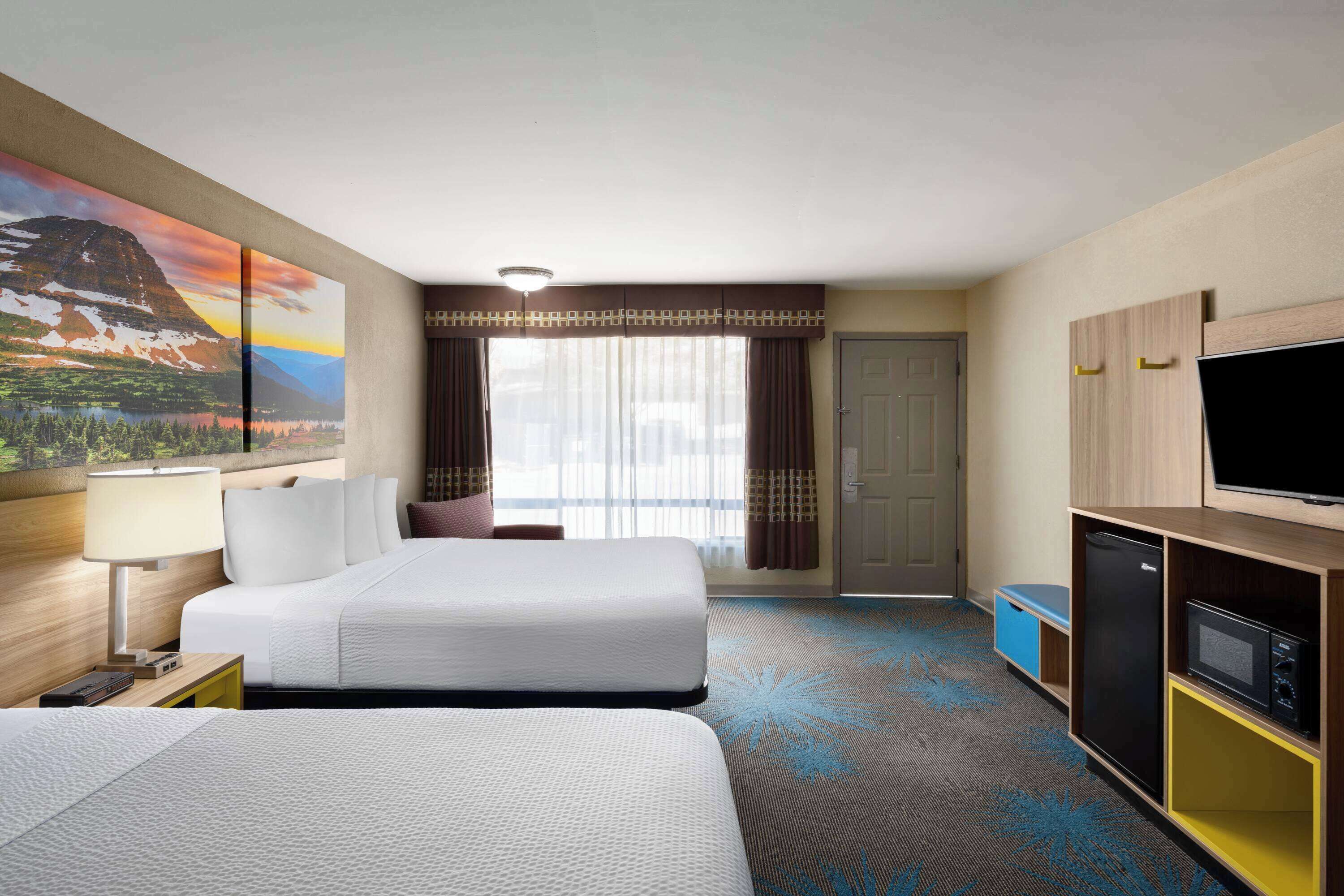 A hotel room with two beds, a TV, a desk, and a window with curtains.