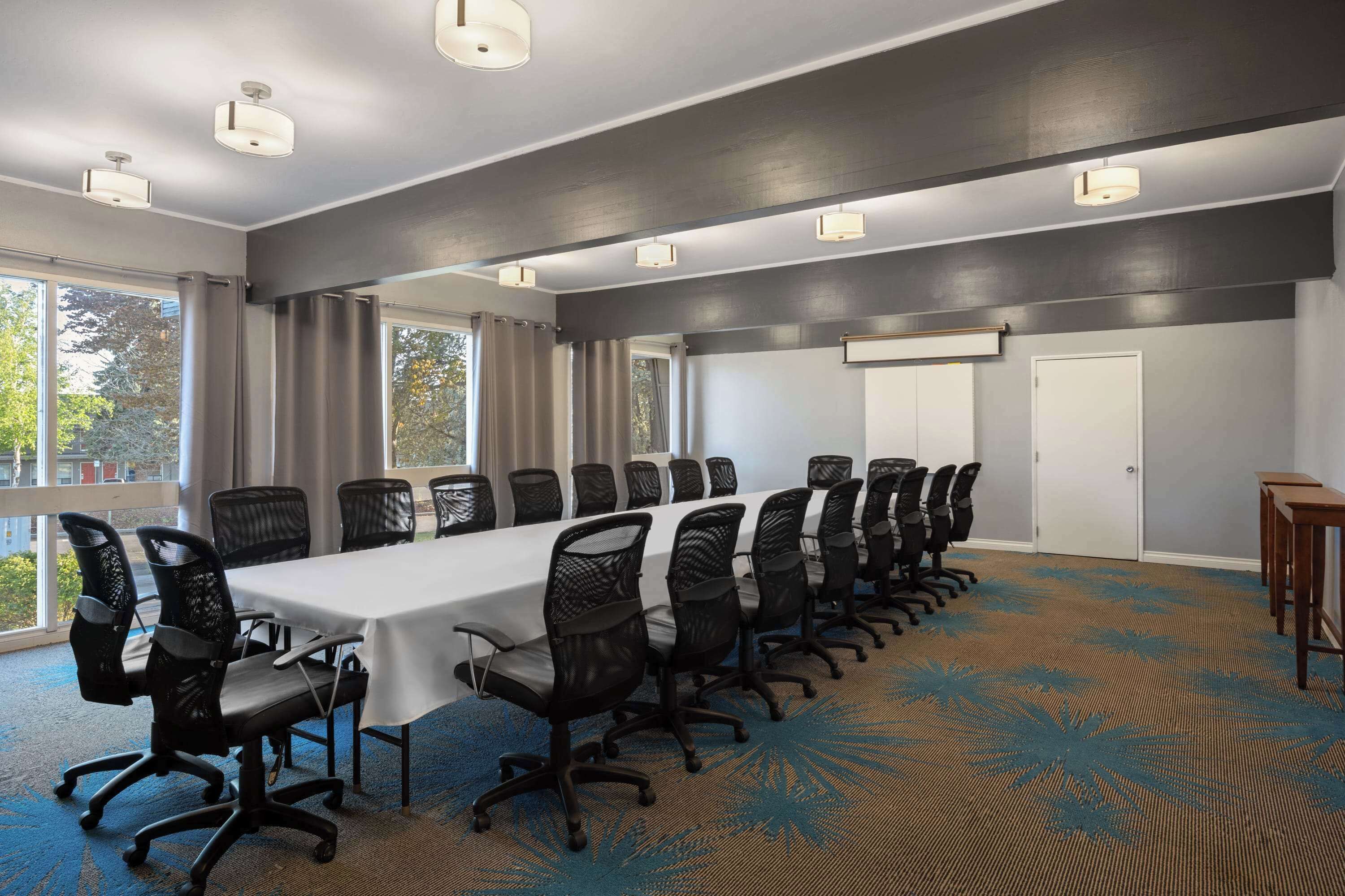 Une salle de conférence avec une longue table, des chaises noires et un sol recouvert de moquette.