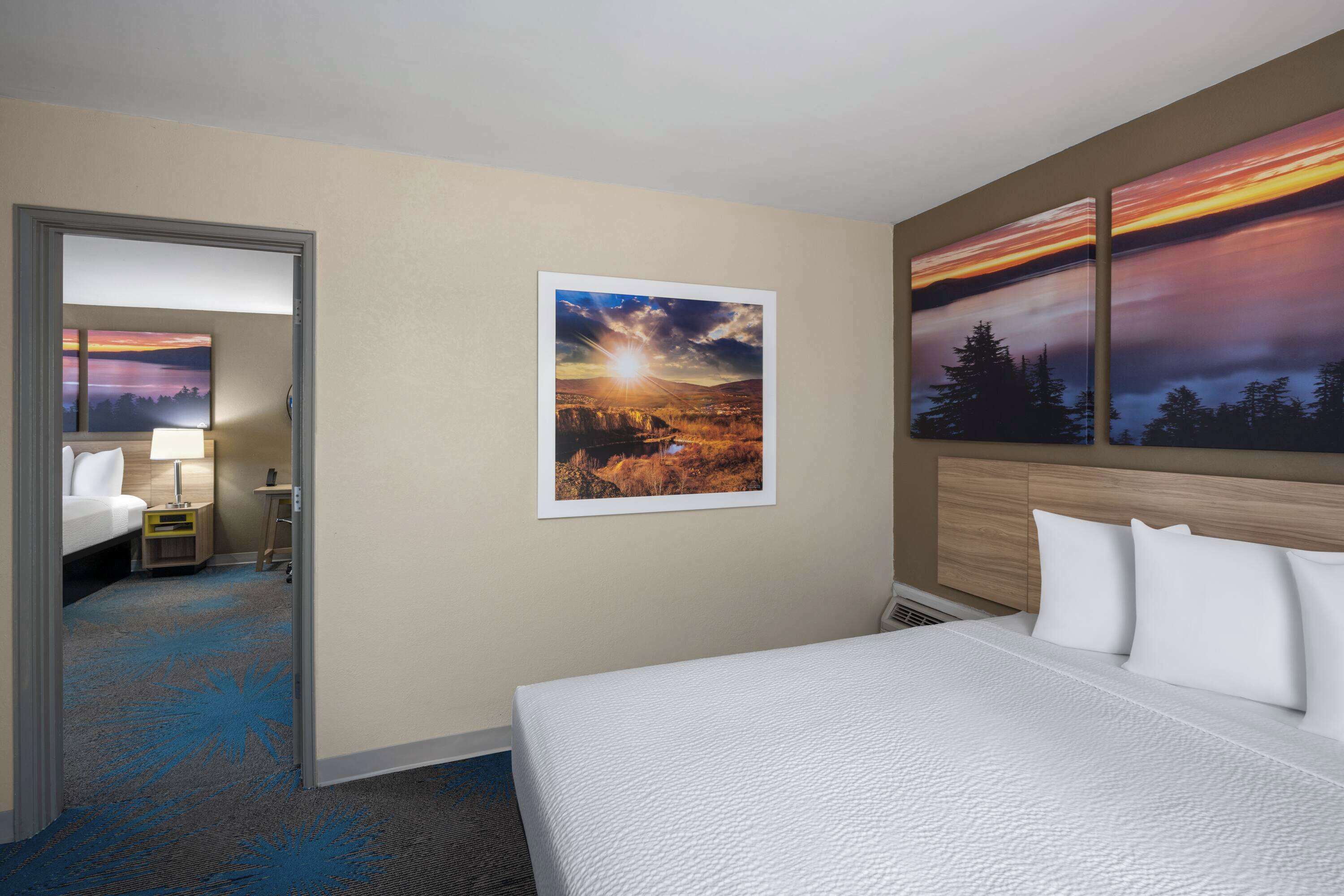 A hotel room with a bed, a nightstand, a lamp, a wall-mounted painting, and a carpet with a blue pattern.