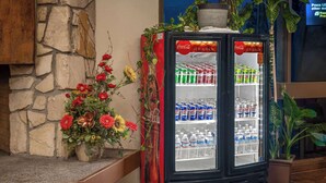 A Coca-Cola refrigerator stocked with beverages, placed next to a flower arrangement.