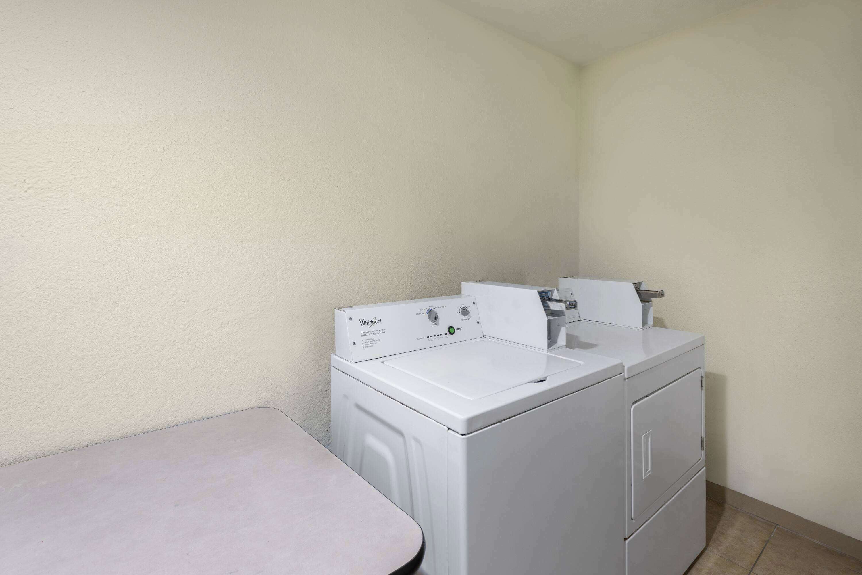 A compact laundry room with a Whirlpool washer and dryer, a small table, and a plain wall.