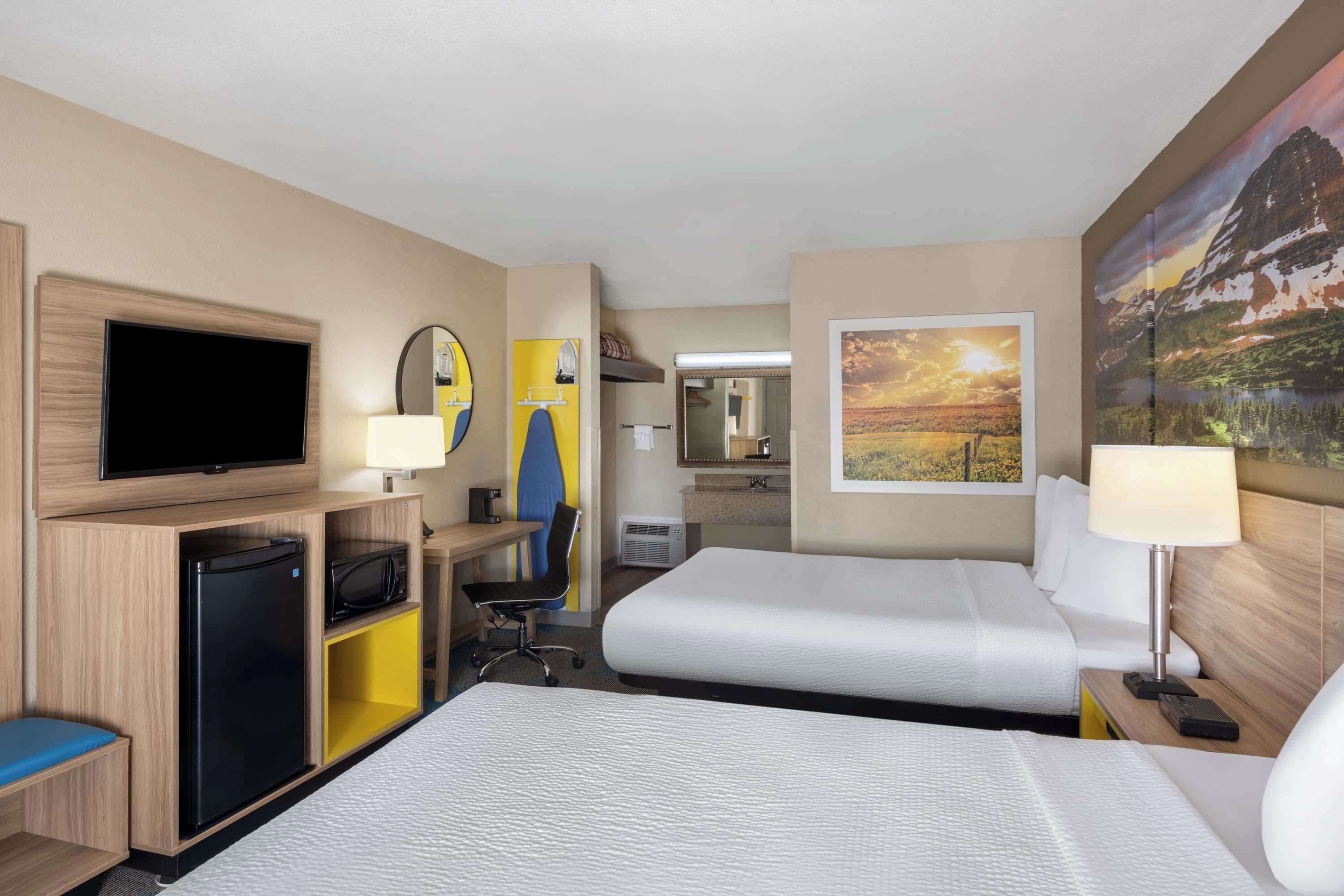 Ein Hotelzimmer mit zwei Betten, einem Fernseher, einem Schreibtisch mit Stuhl, einem kleinen Kühlschrank und einem sichtbaren Badezimmer durch eine offene Tür.