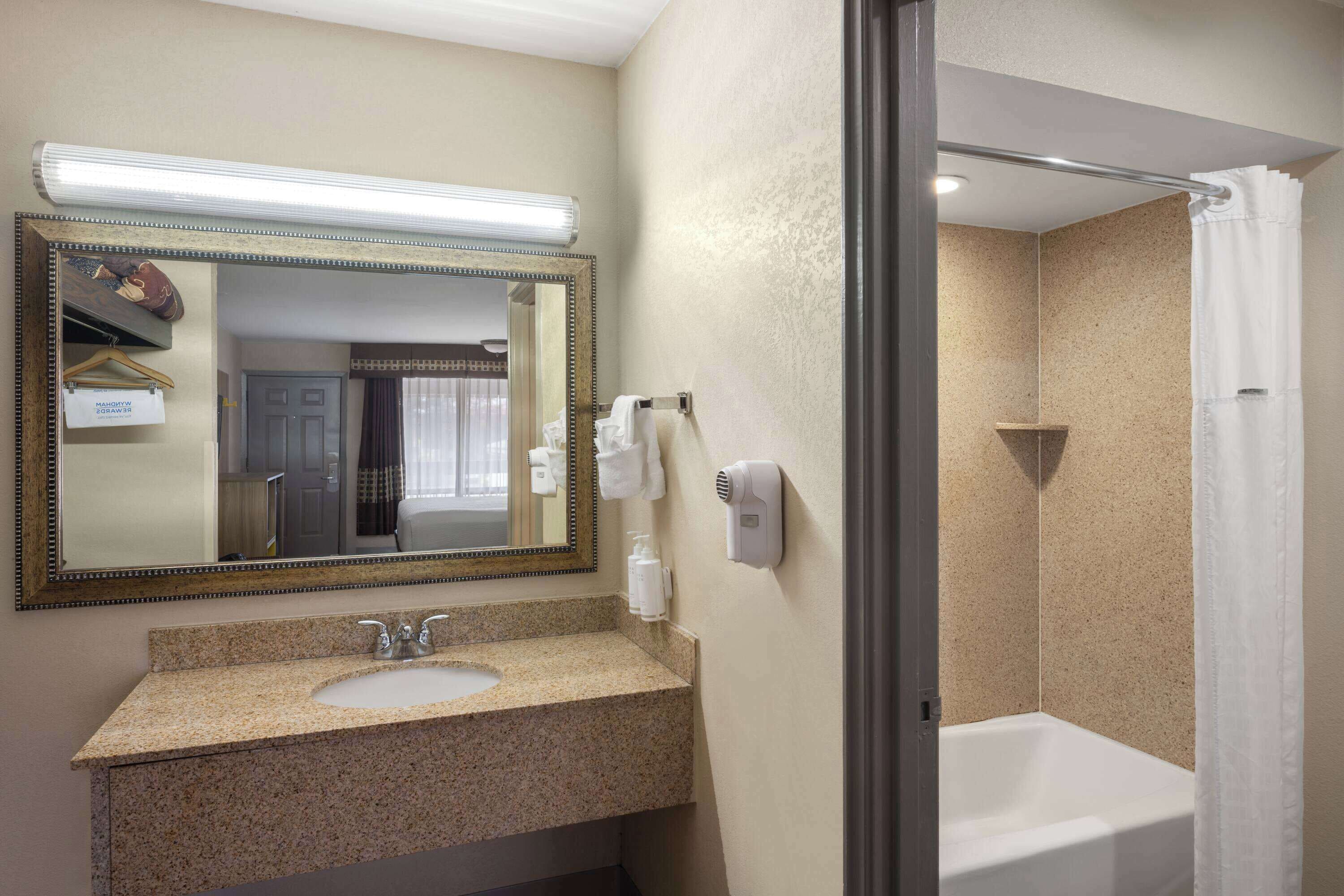 A bathroom with a sink, mirror, towel dispenser, and shower.