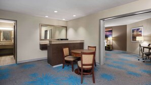 A hotel room with a round table, two chairs, a small desk with a computer, a mirror, and a carpet with a blue pattern.