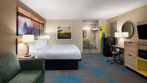 A hotel room with a bed, a desk, a chair, a TV, and a painting on the wall.