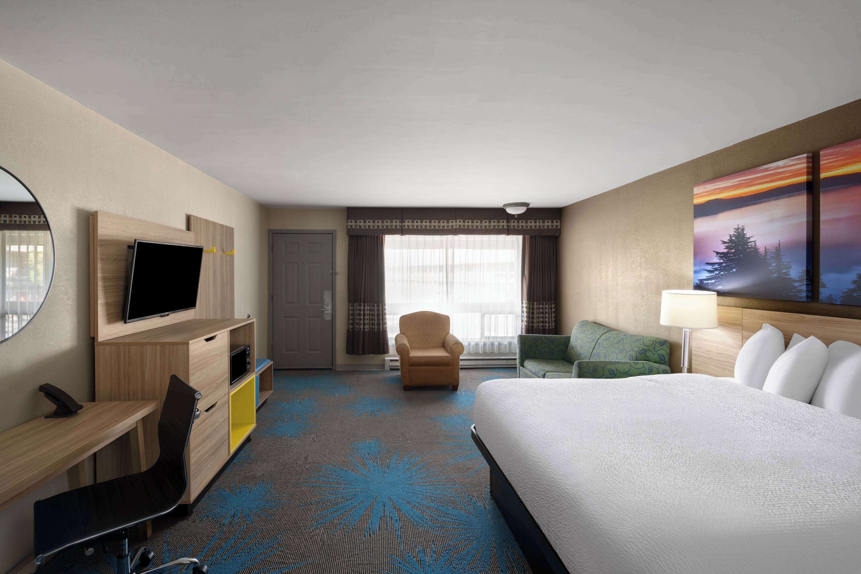 Ein Hotelzimmer mit Bett, Schreibtisch mit Stuhl, Fernseher, Fenster mit Vorhängen und einem Gemälde an der Wand.