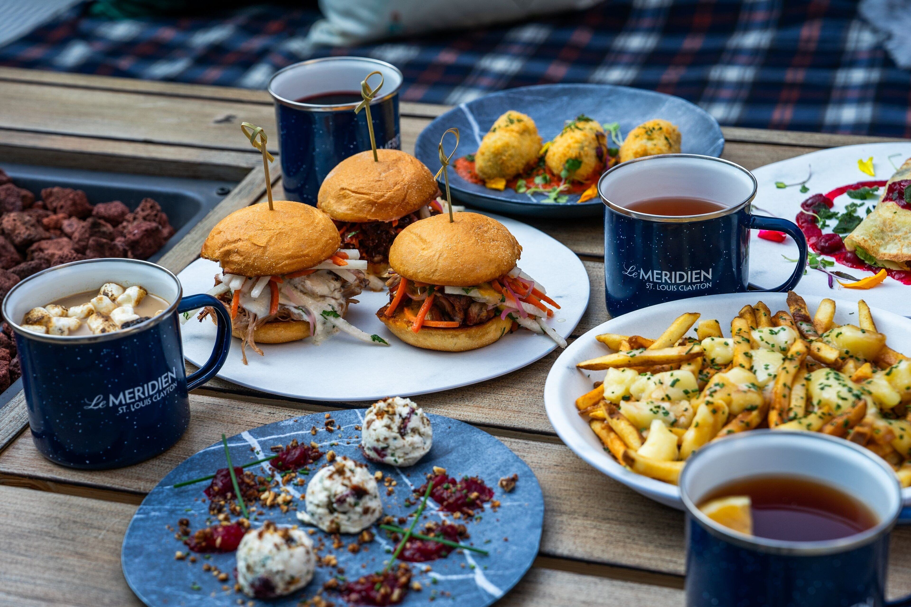 A meal with burgers, fries, and a dessert on a wooden table.