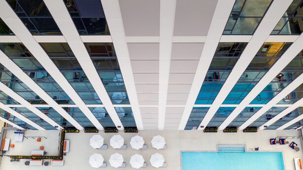A rooftop pool area with multiple lounge chairs and umbrellas, surrounded by a modern building with large windows. - Le Méridien St. Louis Clayton (St. Louis)