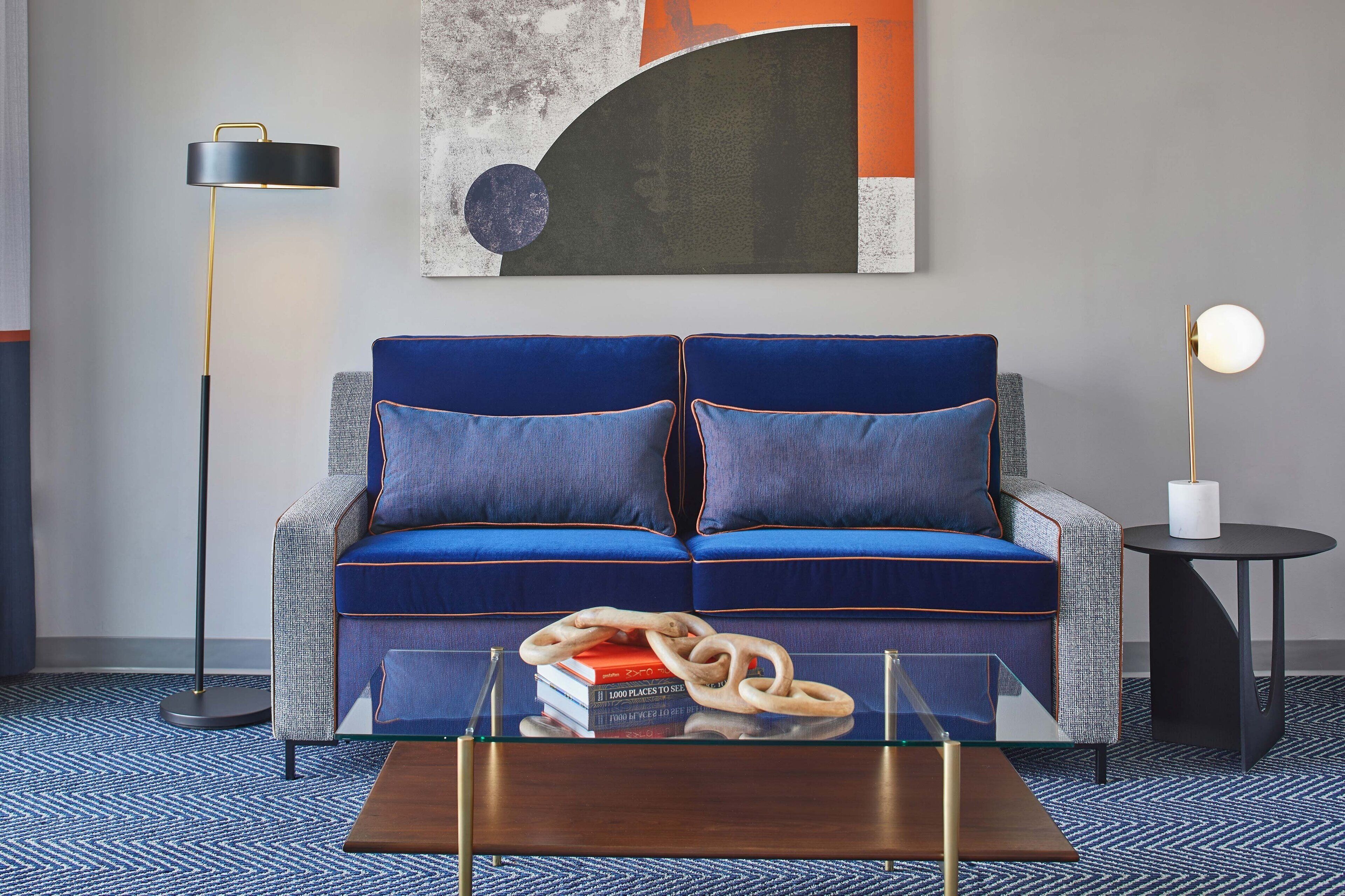 Ein modernes Wohnzimmer mit einem blauen Sofa, einem Glastisch und einer Stehlampe.