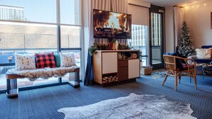 A cozy living room with a large TV, a fireplace, a Christmas tree, and a view of the city. - Le Méridien St. Louis Clayton (St. Louis)
