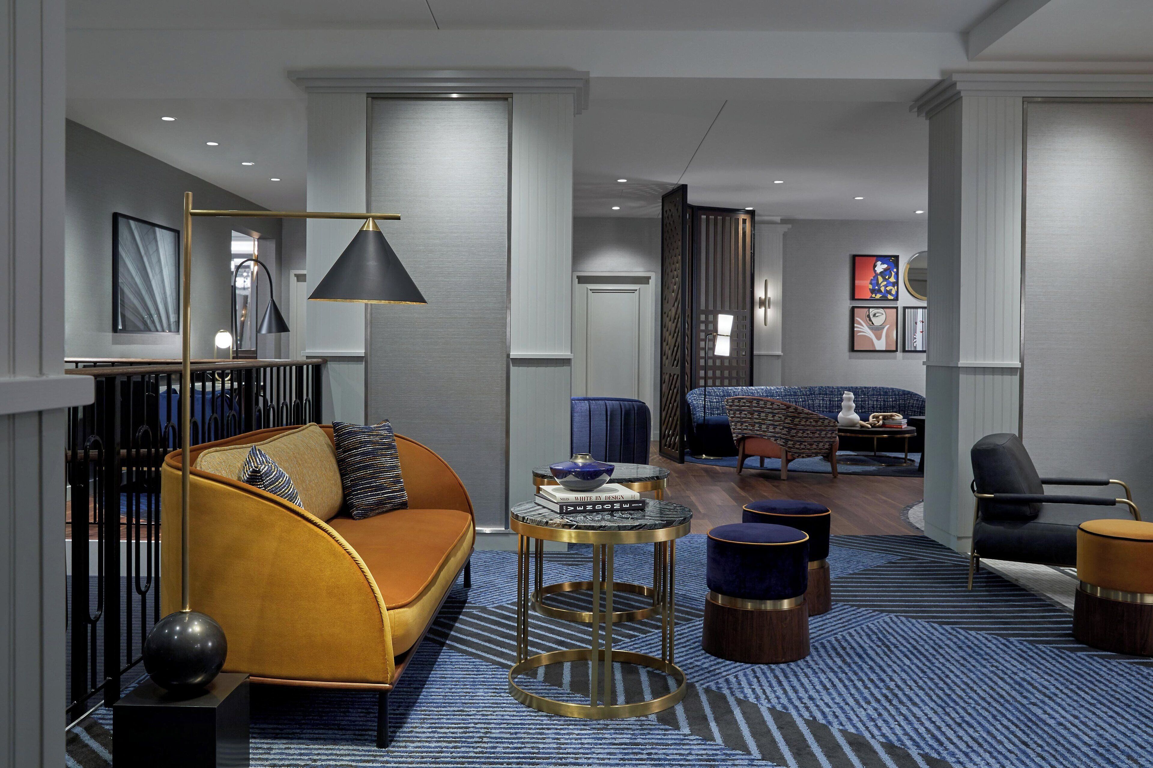 A modern living room with a sofa, coffee table, and ottomans. There is a dining area with a table and chairs in the background.