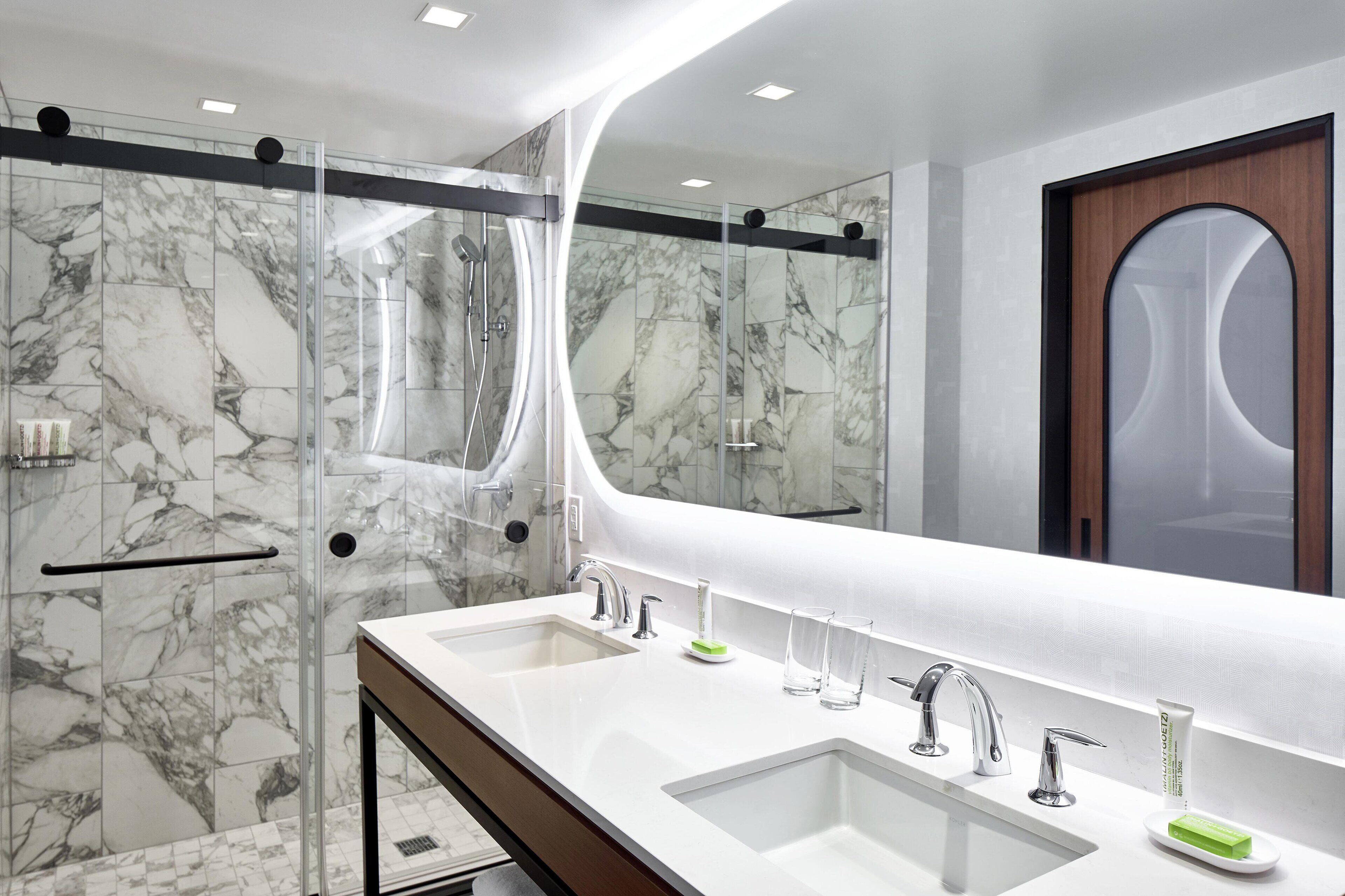 A modern bathroom with a glass-enclosed shower, two sinks with faucets, and a large mirror.