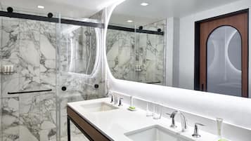 A modern bathroom with a glass-enclosed shower, two sinks with faucets, and a large mirror.