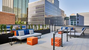 An outdoor seating area with modern furniture, a metal railing, and a view of surrounding buildings. - Le Méridien St. Louis Clayton (St. Louis)