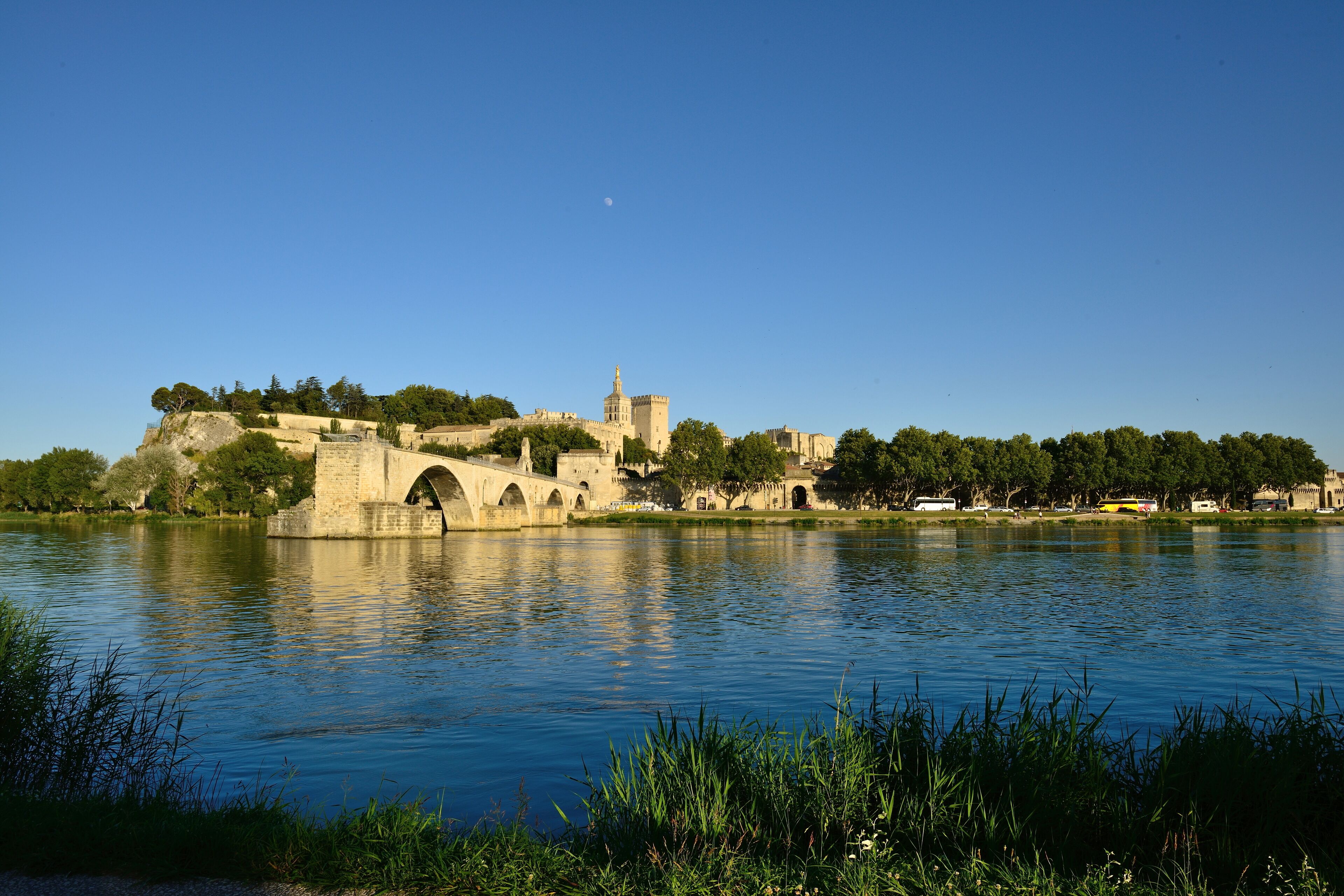 A historic stone bridge over a calm river, surrounded by lush greenery and ancient buildings.