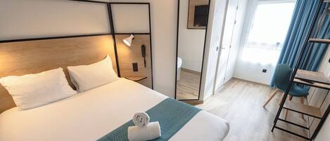 Une chambre d’hôtel avec un grand lit, un bureau, une chaise, un miroir et une fenêtre avec des rideaux.