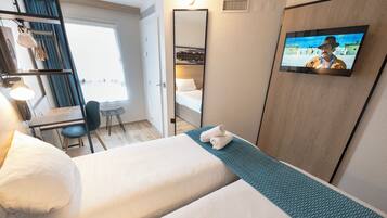 A hotel room with two beds, a desk, a chair, a TV, and a large mirror.