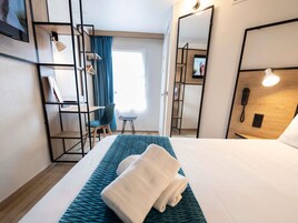 Una habitación de hotel con cama, escritorio, silla, armario y espejo.