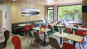 A modern dining area with booths and tables, large windows with a view of greenery, and a cityscape painting on the wall. - ibis Avignon Centre Pont de l'Europe (Avignon)