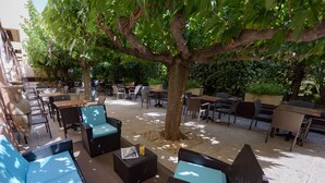 An outdoor seating area with wicker furniture and tables, shaded by a large tree. - ibis Avignon Centre Pont de l'Europe (Avignon)