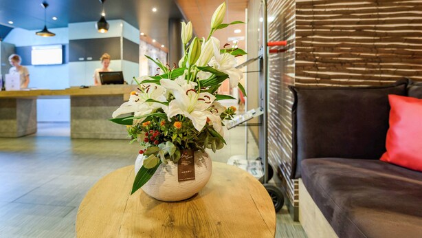 A reception area with a wooden coffee table holding a vase of white lilies. - ibis Avignon Centre Pont de l'Europe (Avignon)