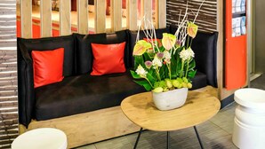 A modern lobby with a black sofa, red cushions, a wooden coffee table, and a potted plant with flowers. - ibis Avignon Centre Pont de l'Europe (Avignon)