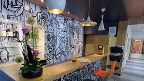 A bar area with a wooden counter, black and white wall art, and orange chairs. - ibis Avignon Centre Pont de l'Europe (Avignon)