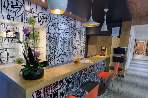 A bar area with a wooden counter, black and white wall art, and orange chairs. - ibis Avignon Centre Pont de l'Europe (Avignon)