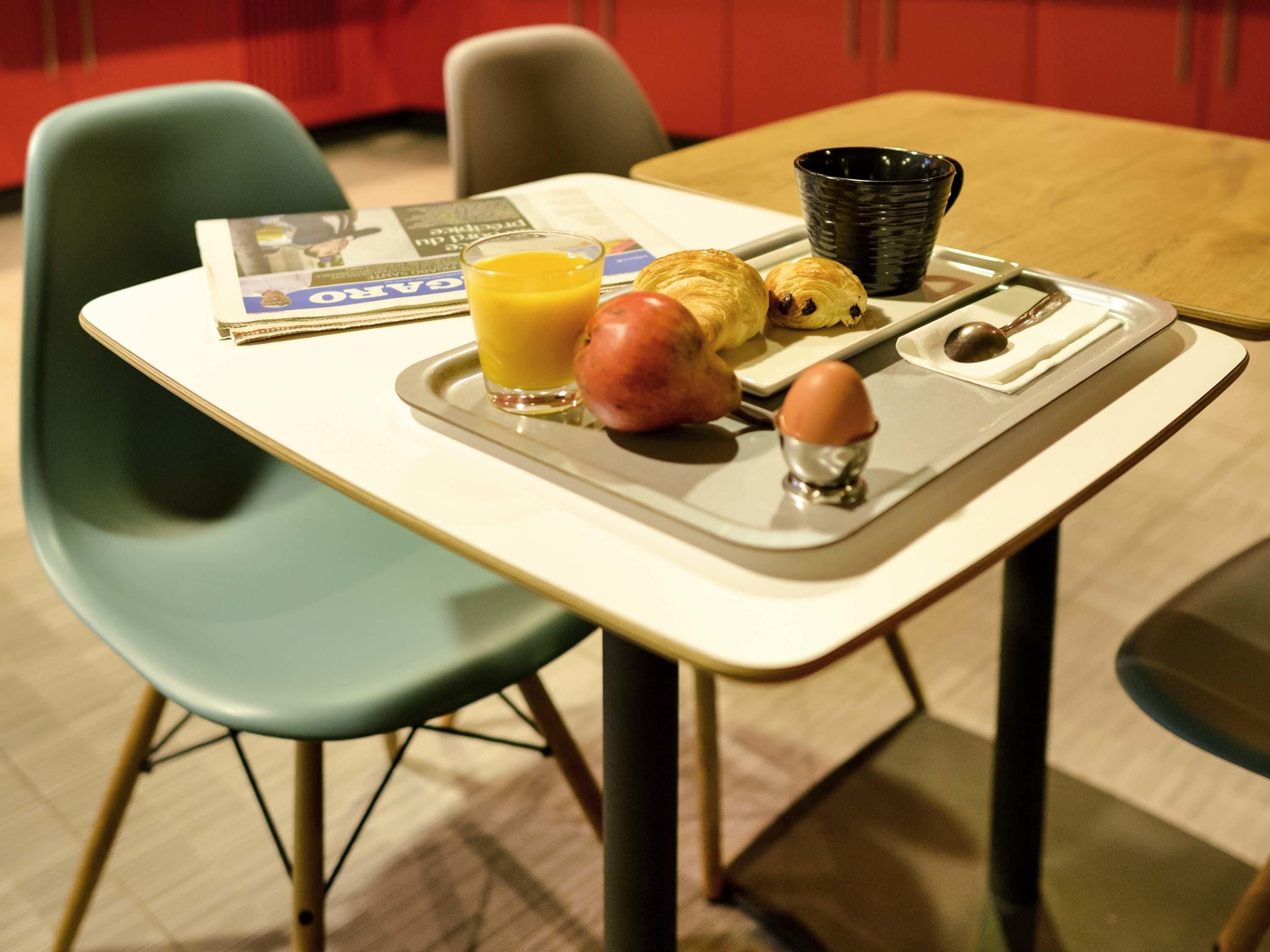 A breakfast tray with croissants, an apple, a glass of orange juice, and a cup on a table.