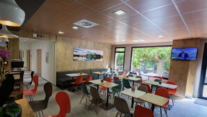 A modern dining area with multiple tables and chairs, a television on the wall, and a view of the outdoors through large windows. - ibis Avignon Centre Pont de l'Europe (Avignon)