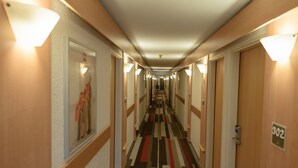 A hotel hallway with carpeted floors, doors on both sides, and wall-mounted light fixtures. - ibis Avignon Centre Pont de l'Europe (Avignon)