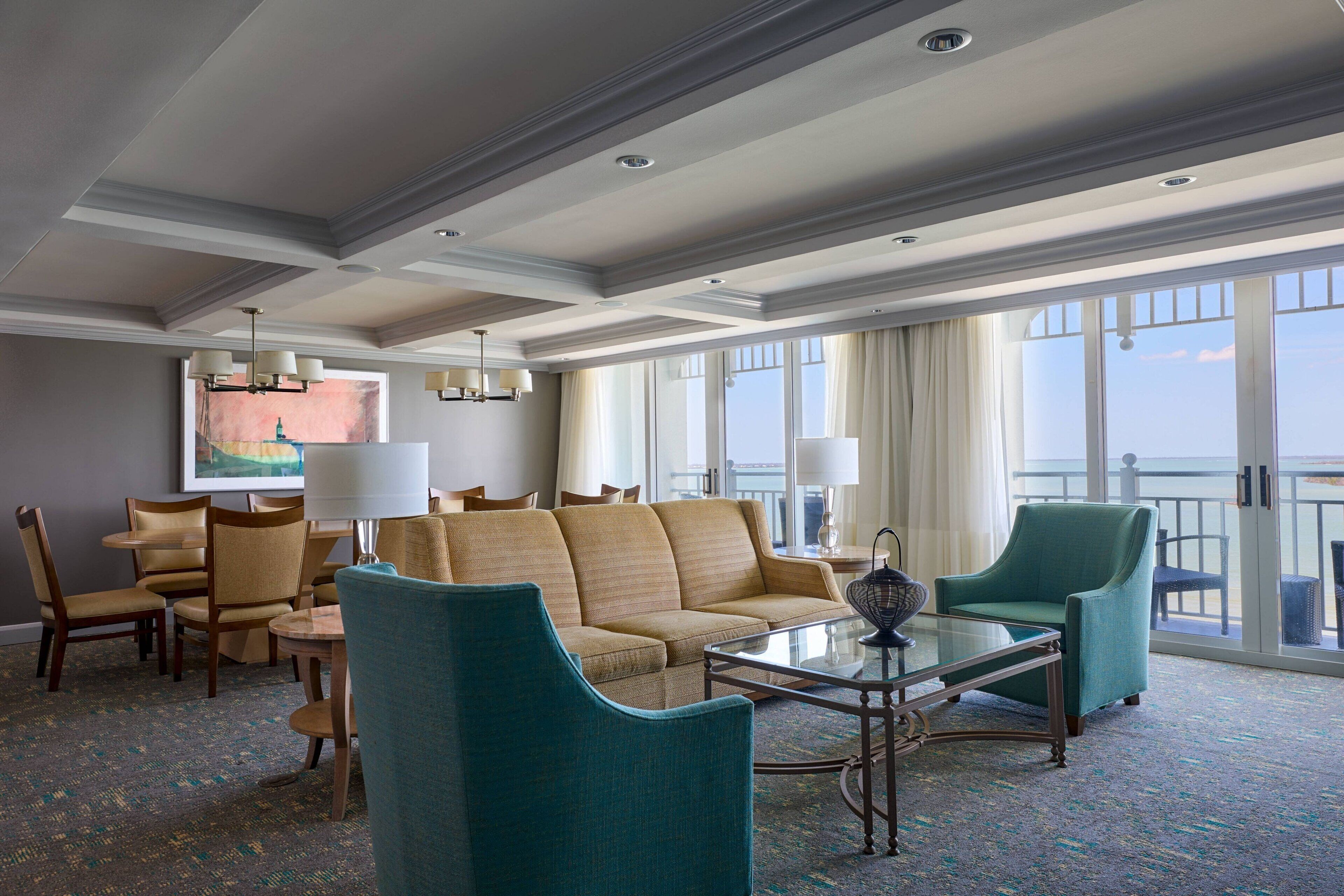 A spacious hotel lobby with a large sofa, armchairs, a coffee table, and a painting on the wall.