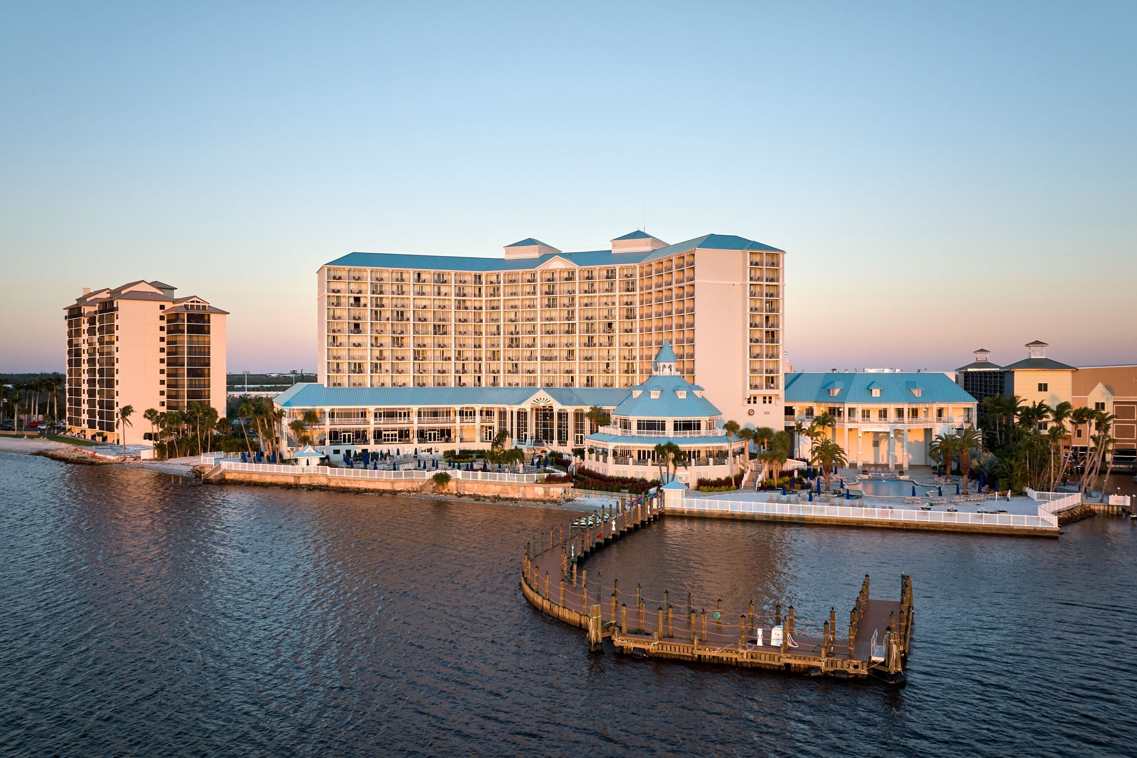 A large hotel with multiple floors and a central dome structure, located near a waterfront with a dock.