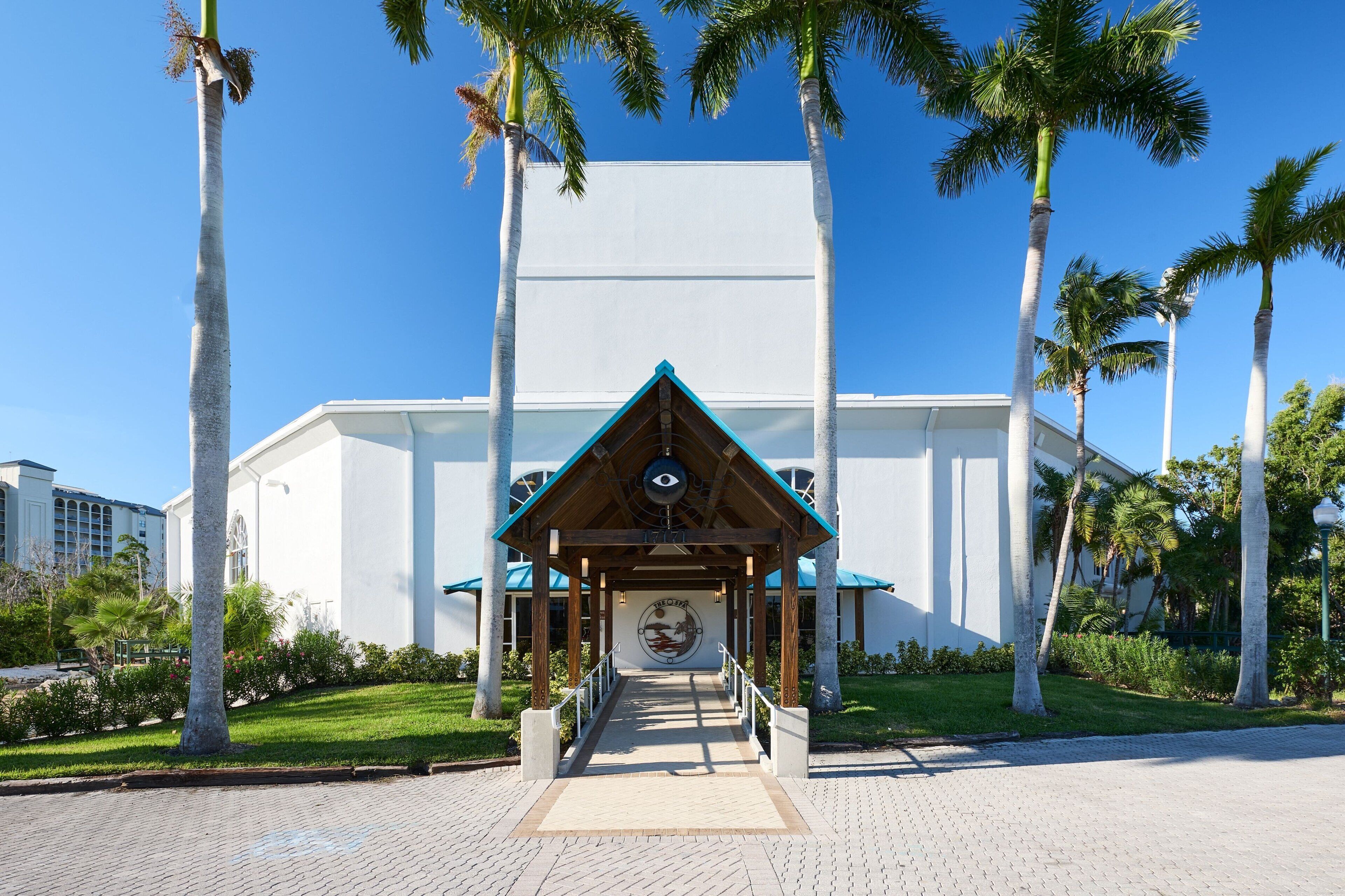 A building with a covered entrance, palm trees, and a clear blue sky.