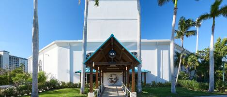 A building with a covered entrance, palm trees, and a clear blue sky.
