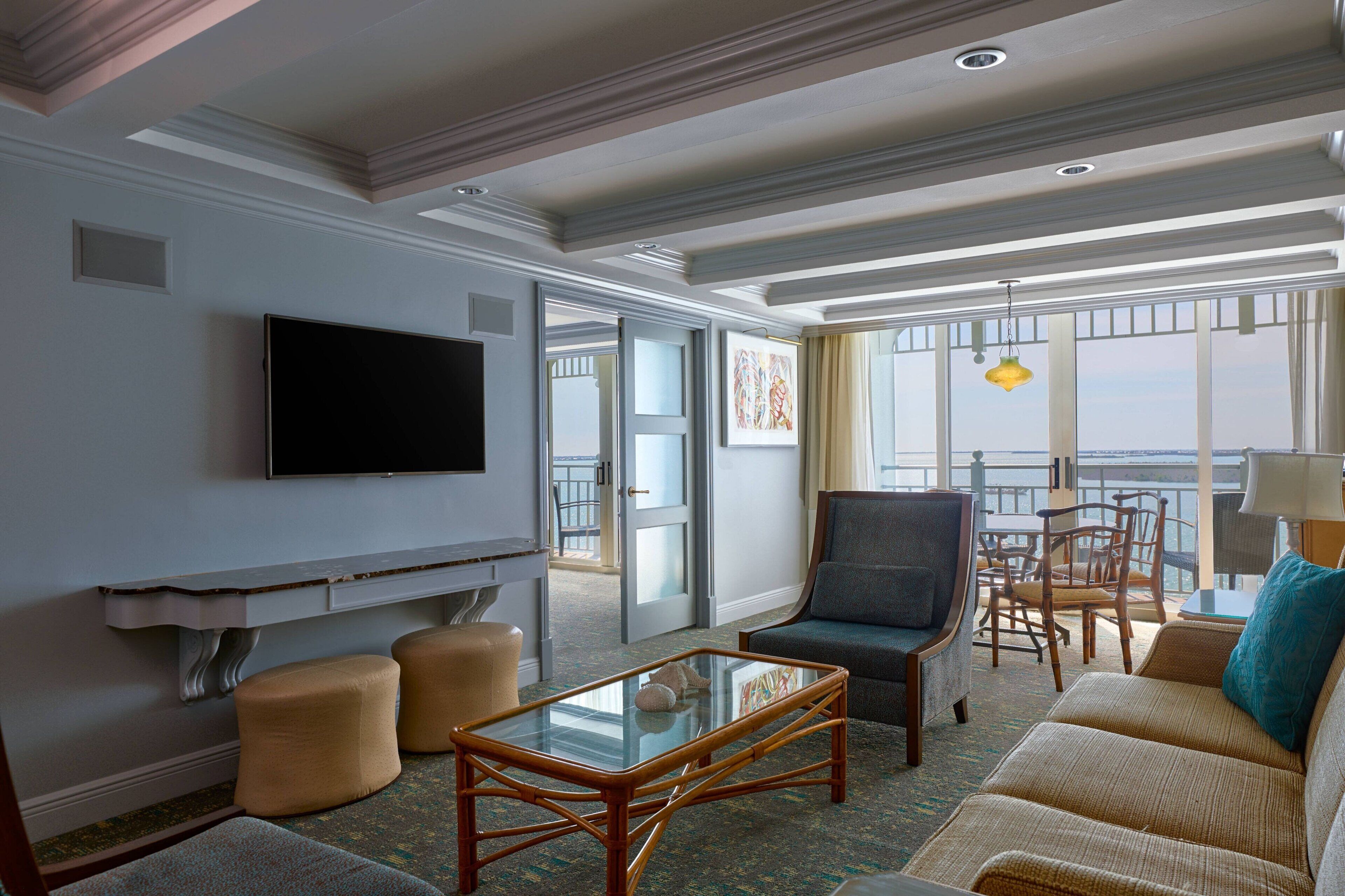 Habitación de hotel con televisión de pantalla plana, asientos cómodos, una mesa de centro de vidrio y ventanas amplias con vistas.