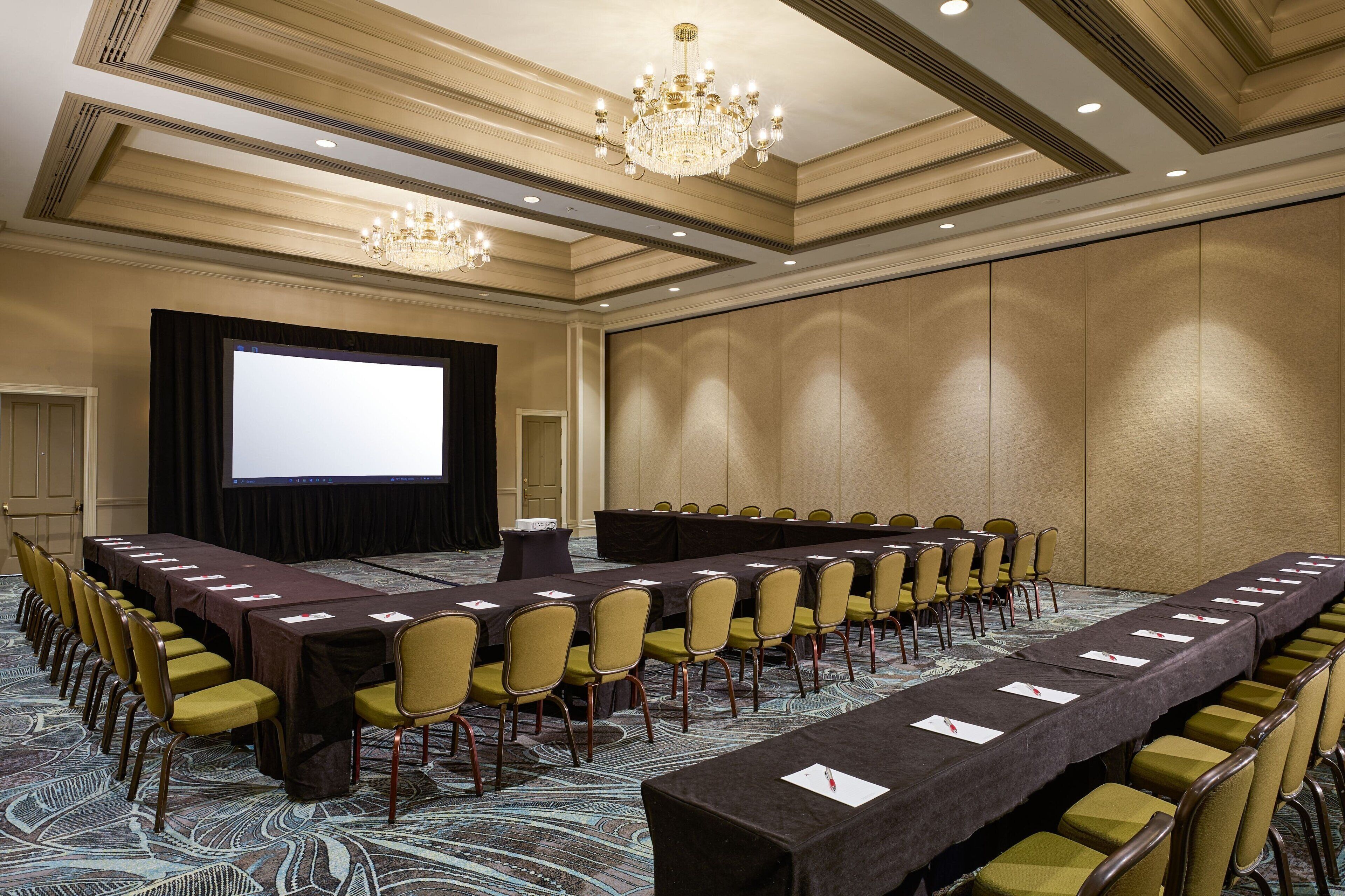 A conference room with a long table, chairs, a projector screen, and a chandelier.