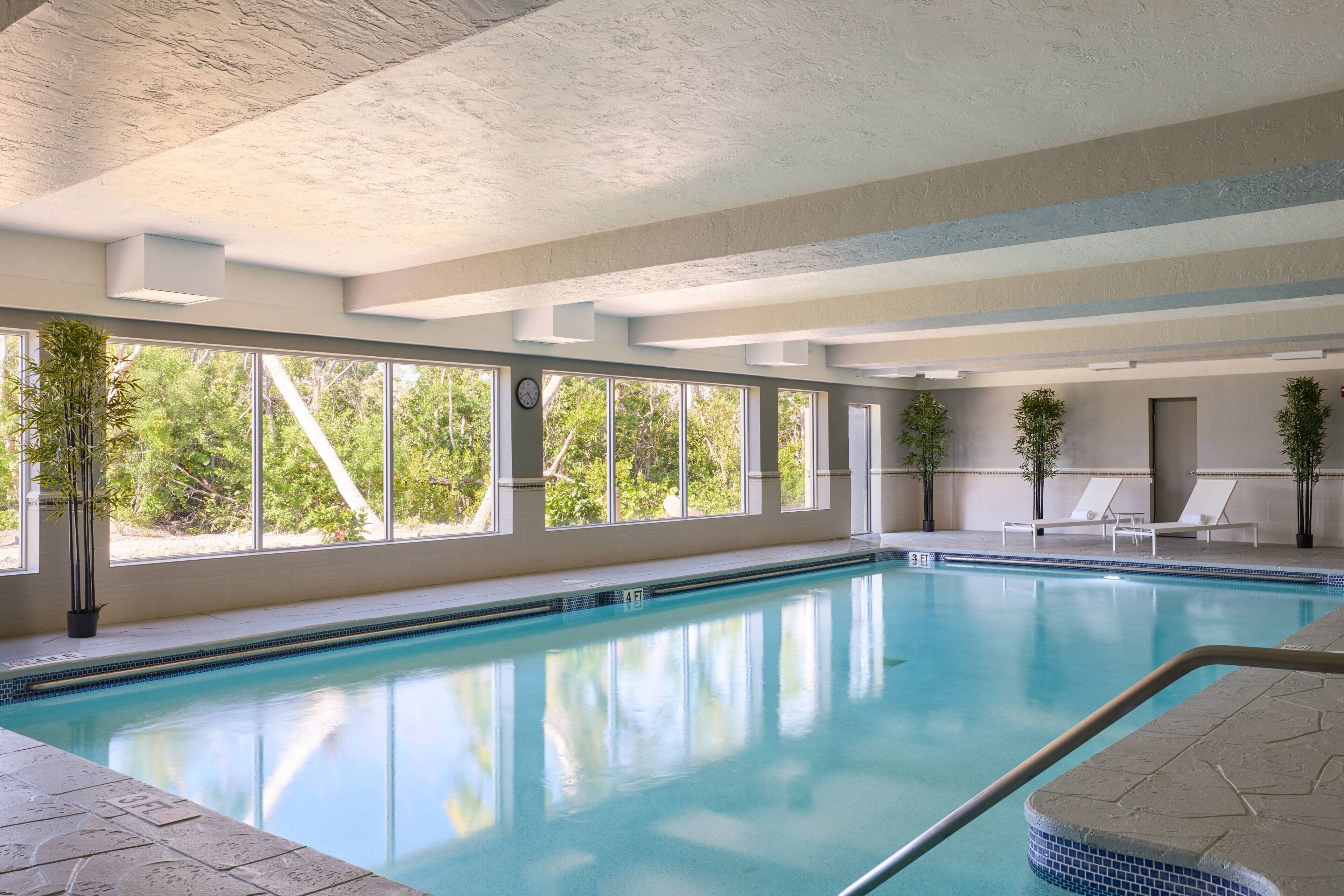 An indoor swimming pool with clear glass walls, a tiled floor, and a few lounge chairs.