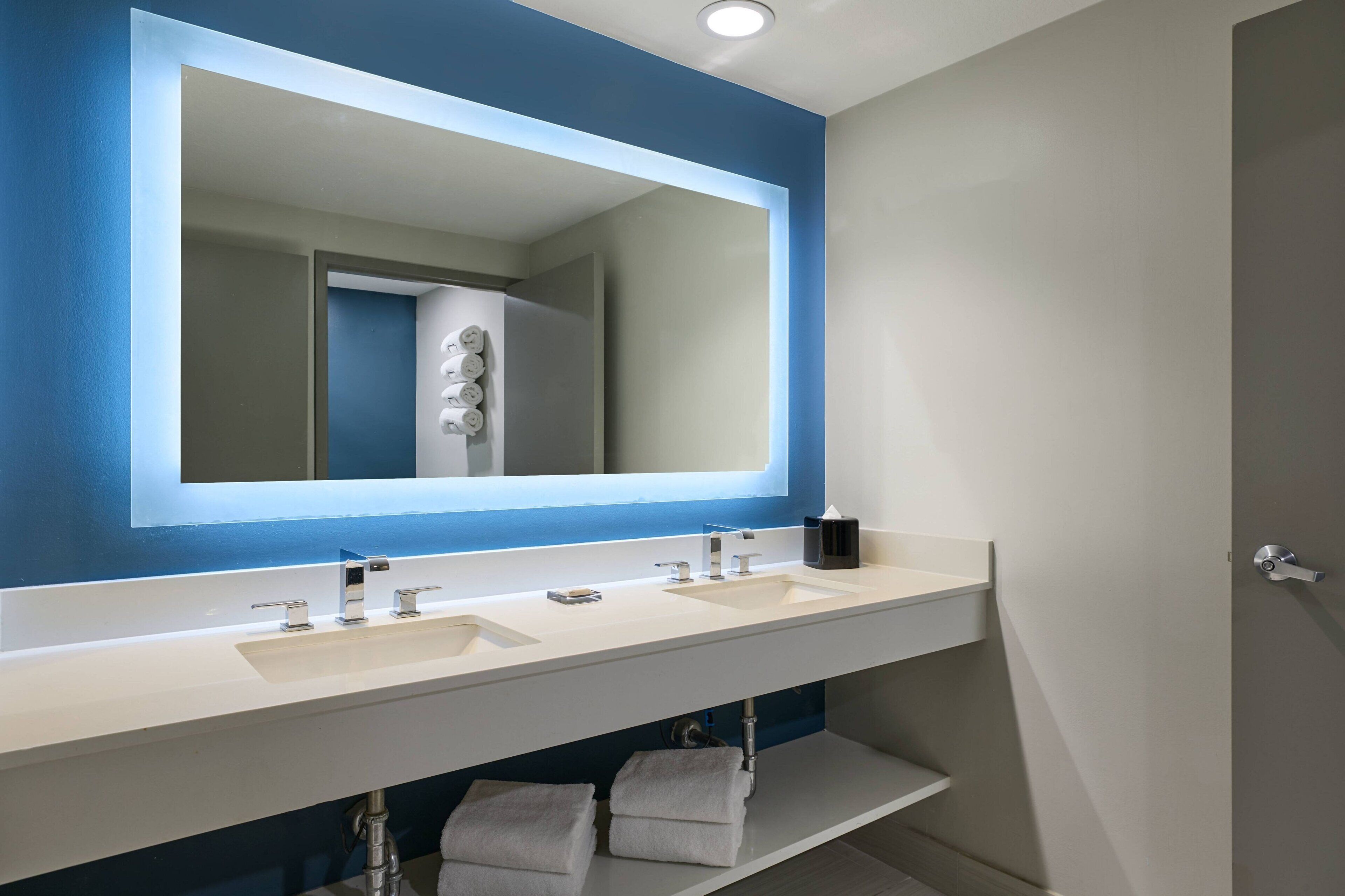 A modern bathroom with a large mirror, two sinks, and a towel rack.