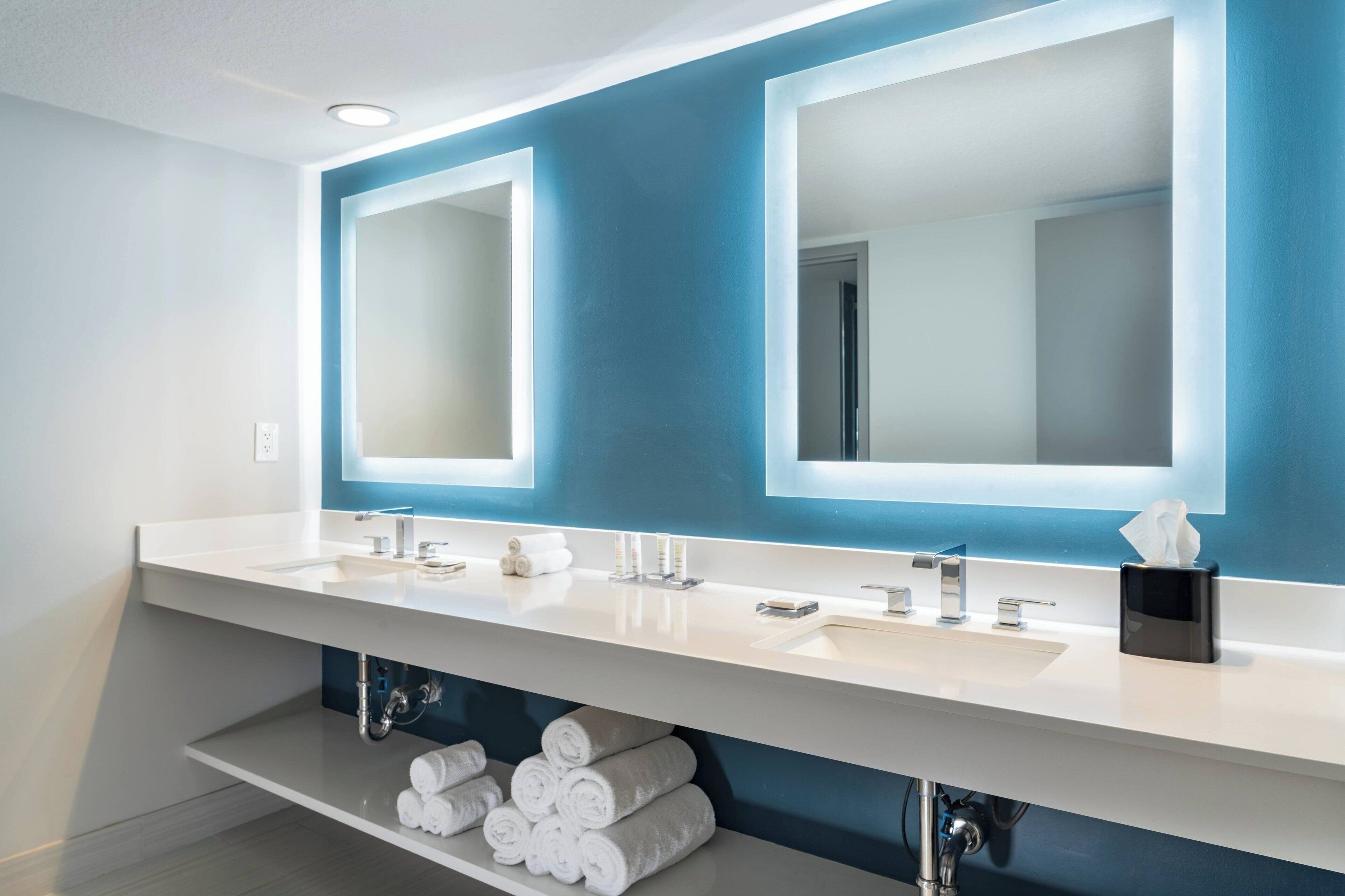 A modern bathroom with a white sink, double mirrors, and a towel rack.